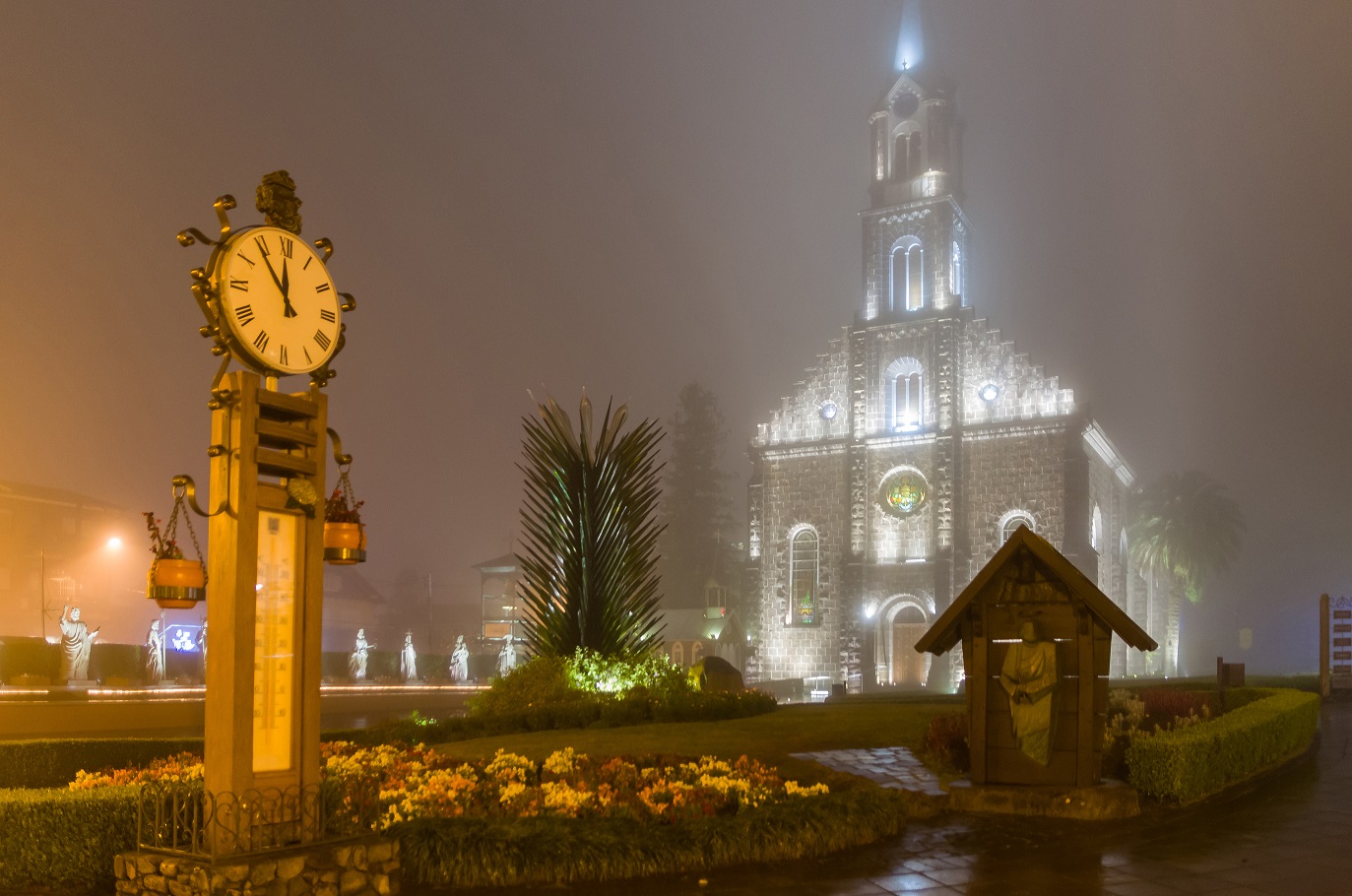 Imagem dos termômetros de Gramado durante a noite, ao fundo, a Igreja Matriz de São Iluminada e desfocada devido a neblina