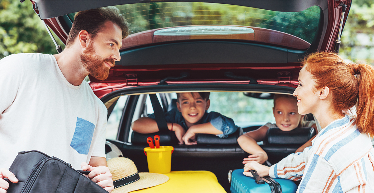 Casal e dois filhos prontos para viajar com as malas no porta-malas do carro